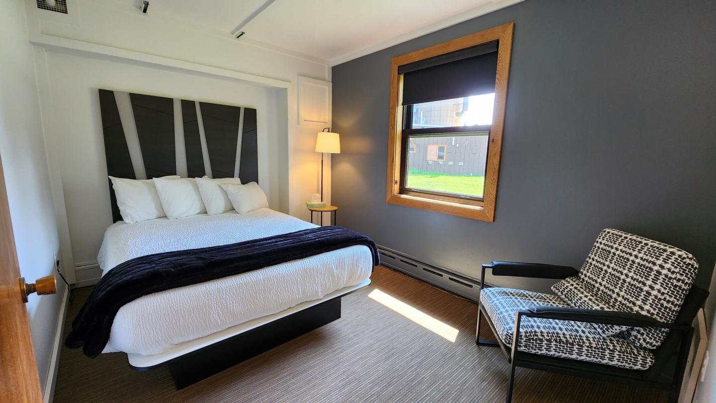 Cozy bedroom with a bed, armchair, and lamp by a window.