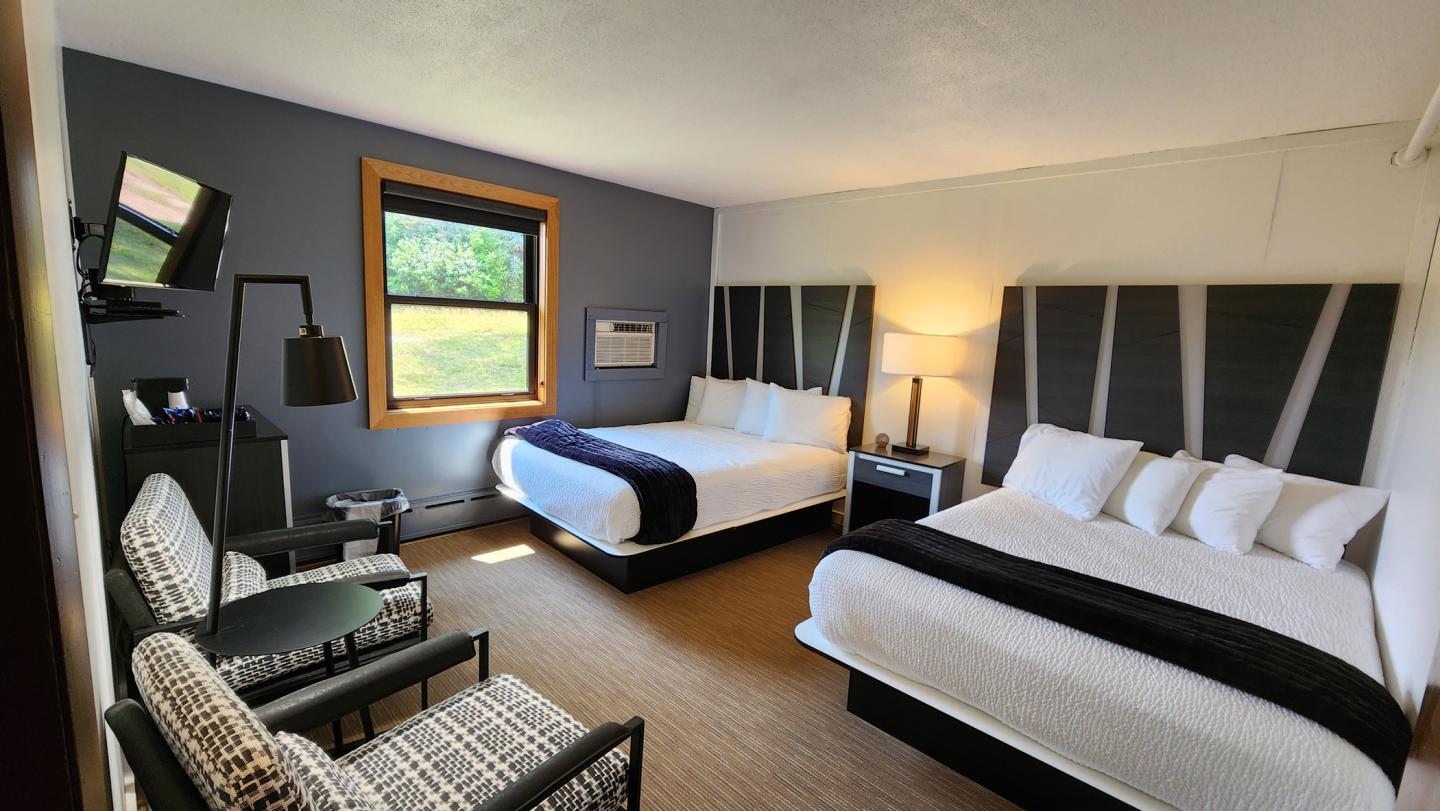 Hotel room with two double beds, a window, chairs, and a floor lamp.