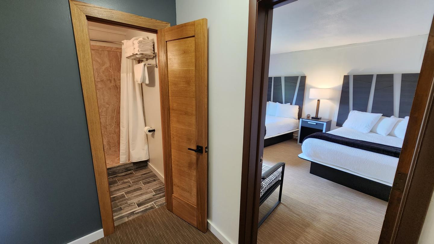Hotel room with two beds, adjoining bathroom with shower curtain.