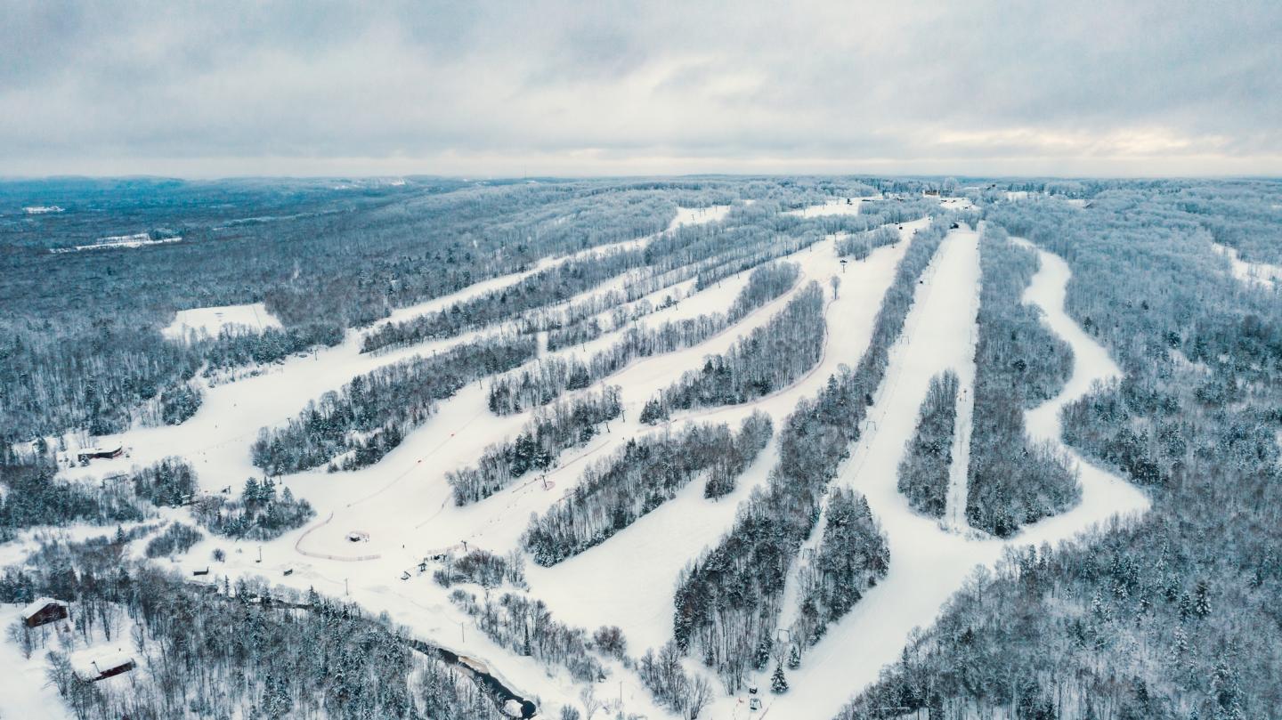 Snow-covered ski resort with multiple trails winding through a forested landscape.