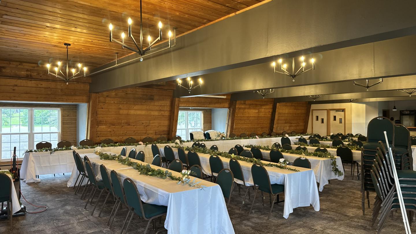 Banquet room with decorated tables and chairs, warm lighting from chandeliers.