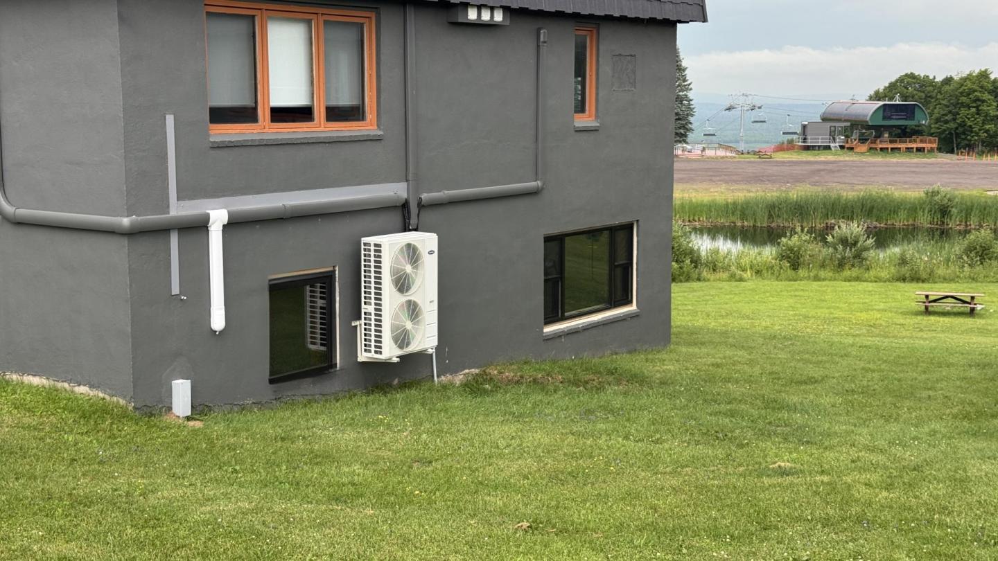 Gray house on grassy hill with lake in background.