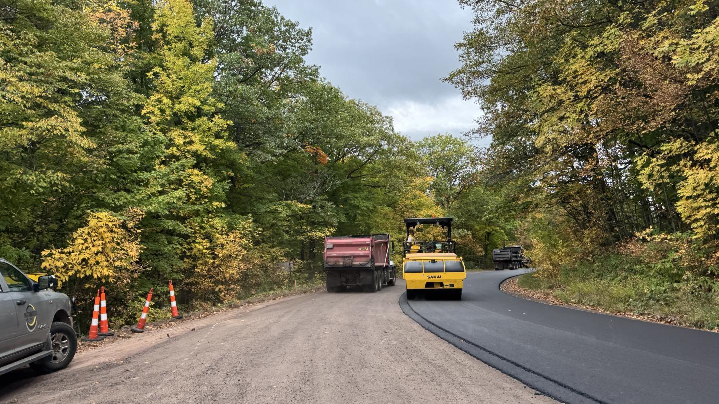Paved road under construction with trees on both sides.