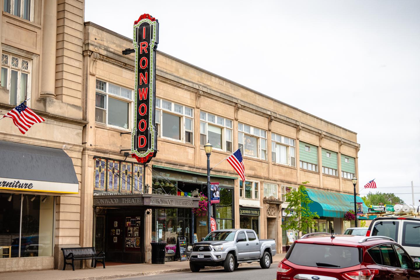 Historic theater on a small-town street with parked cars and flags.