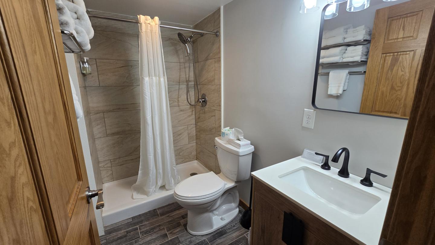 Bathroom with a shower, toilet, and sink, featuring wooden accents and a white curtain.