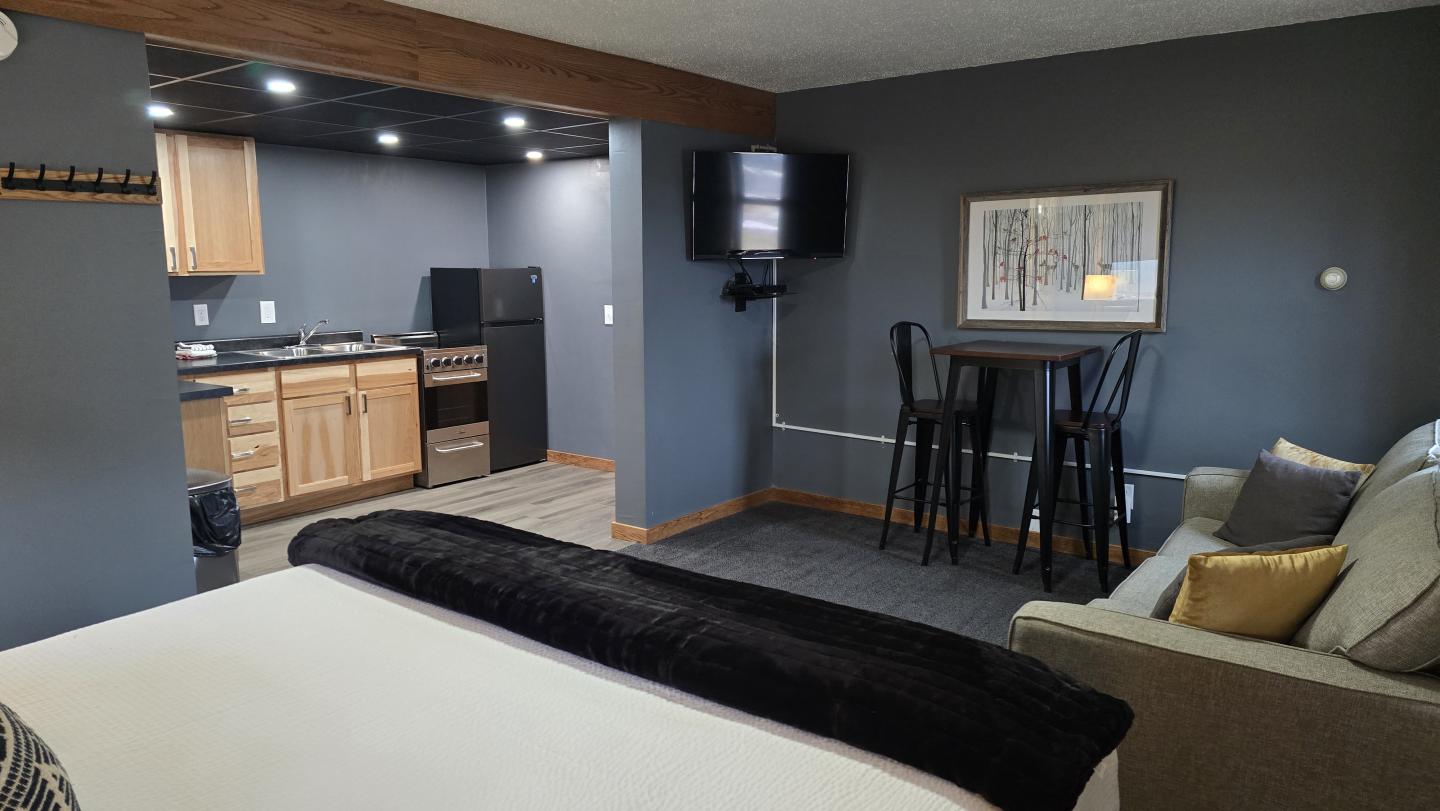 Cozy hotel room with kitchenette, sofa, bed, and small dining area in neutral tones.