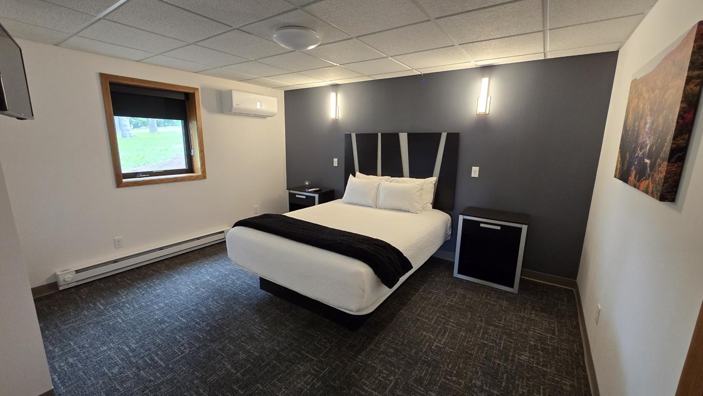 Modern hotel room with a bed, dark accent wall, and soft lighting.