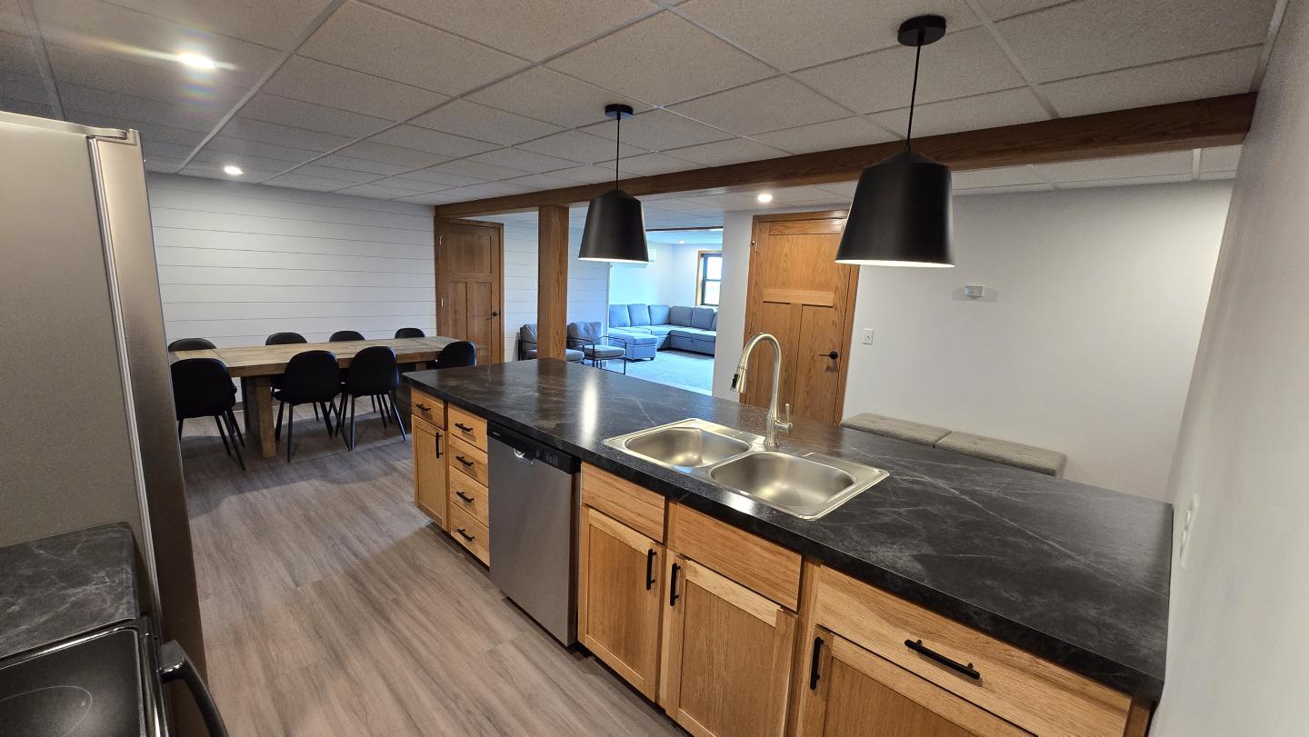 Modern kitchen with wood cabinets, black countertops, and pendant lights.