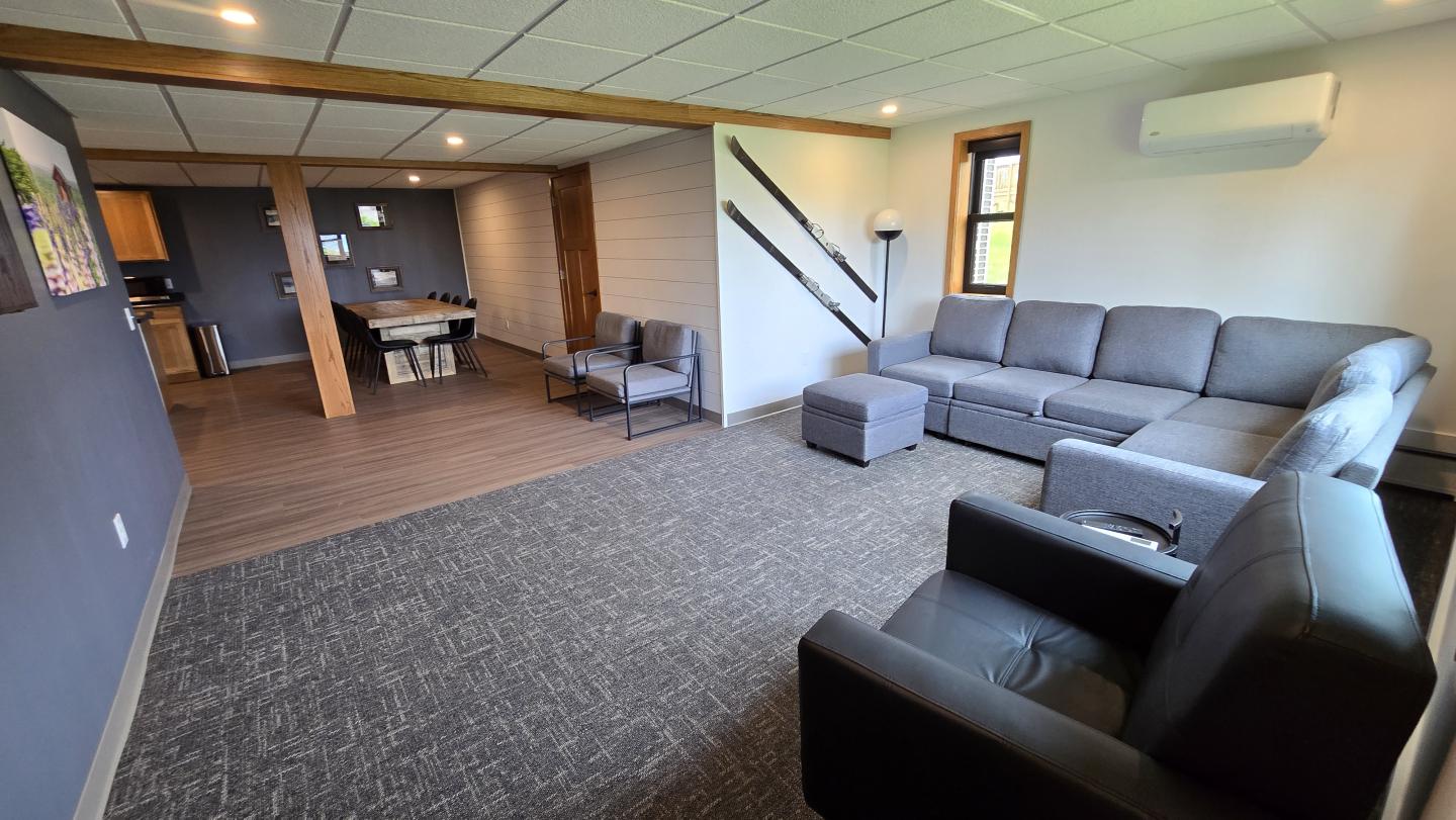 Spacious living room with gray sofas, armchairs, and a dining area in the background.