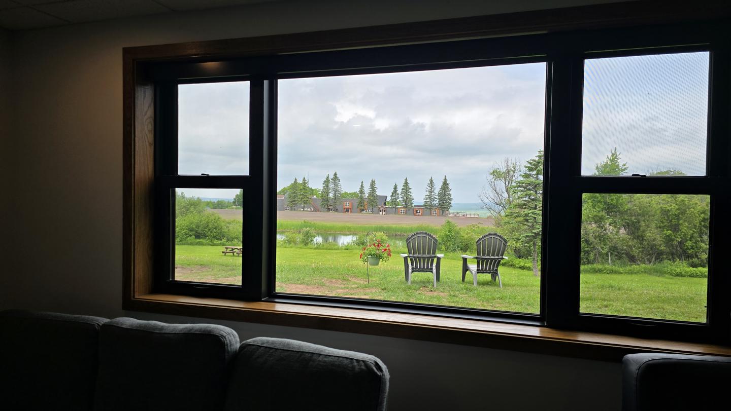 View of a grassy field through a large window with two chairs outside.