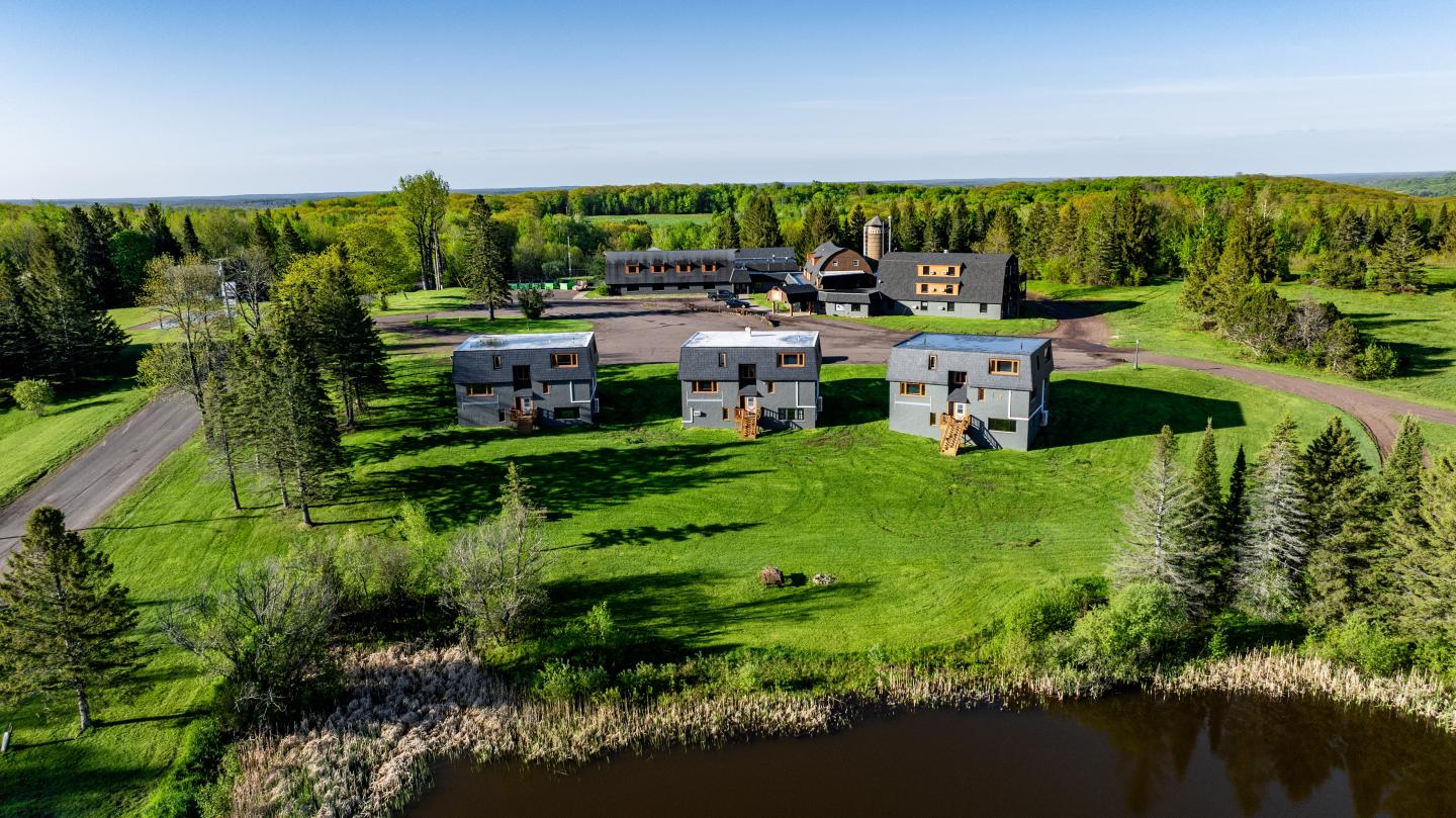 Aerial view of cabins surrounded by lush green landscape near a pond.