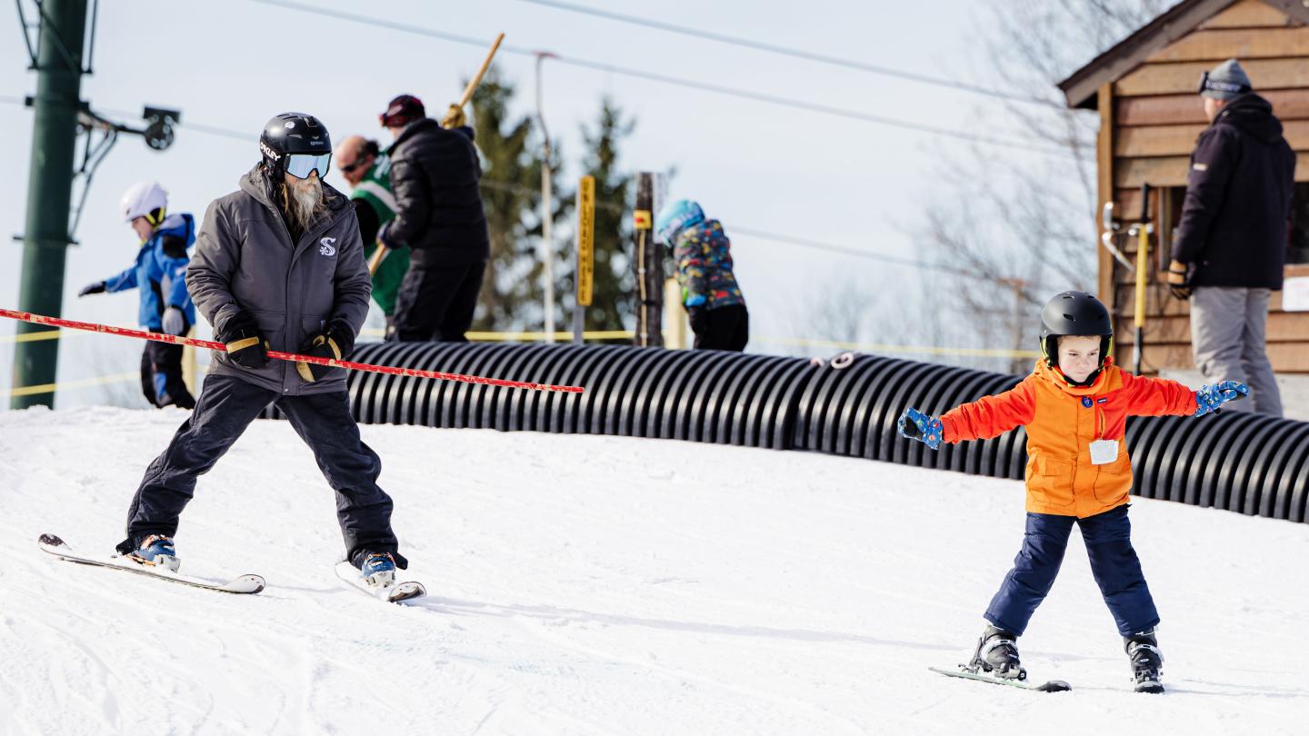 Adult and child skiing downhill in snow.
