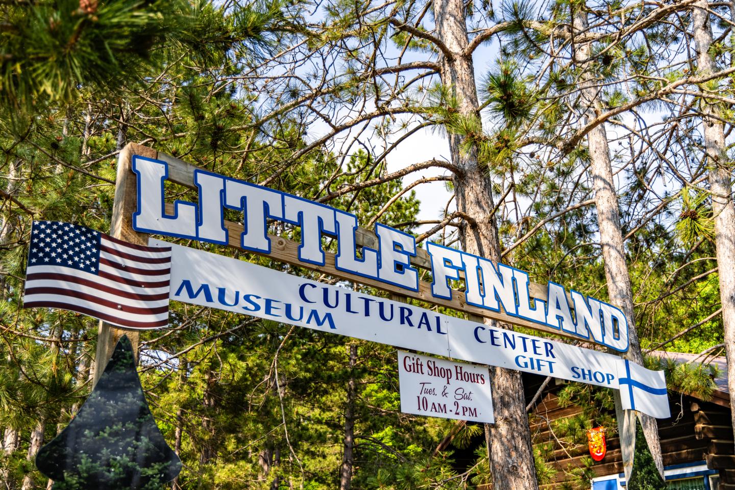 Little Finland sign with American and Finnish flags, surrounded by pine trees.