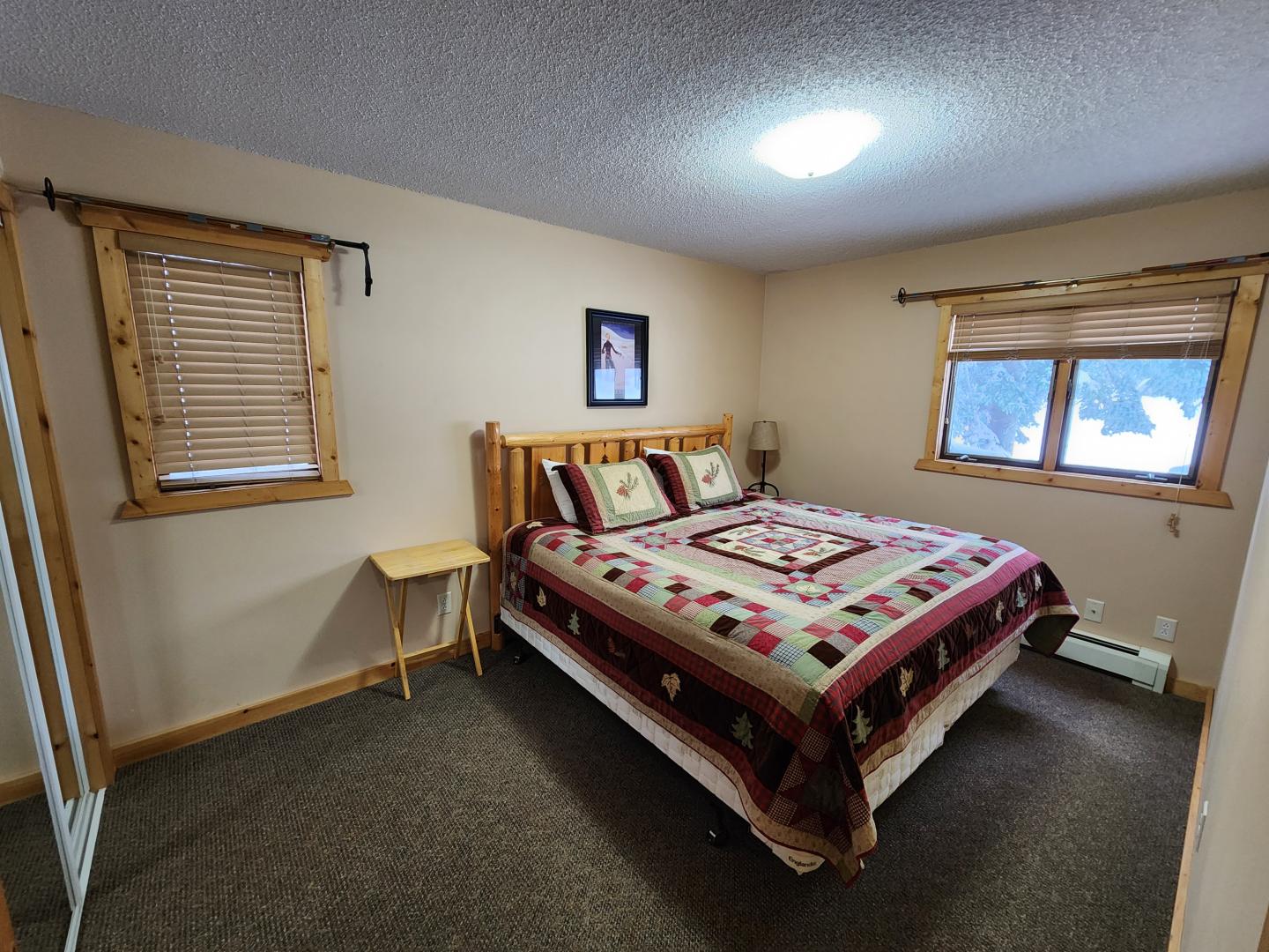 Cozy bedroom with a large bed, wooden furniture, and two windows.