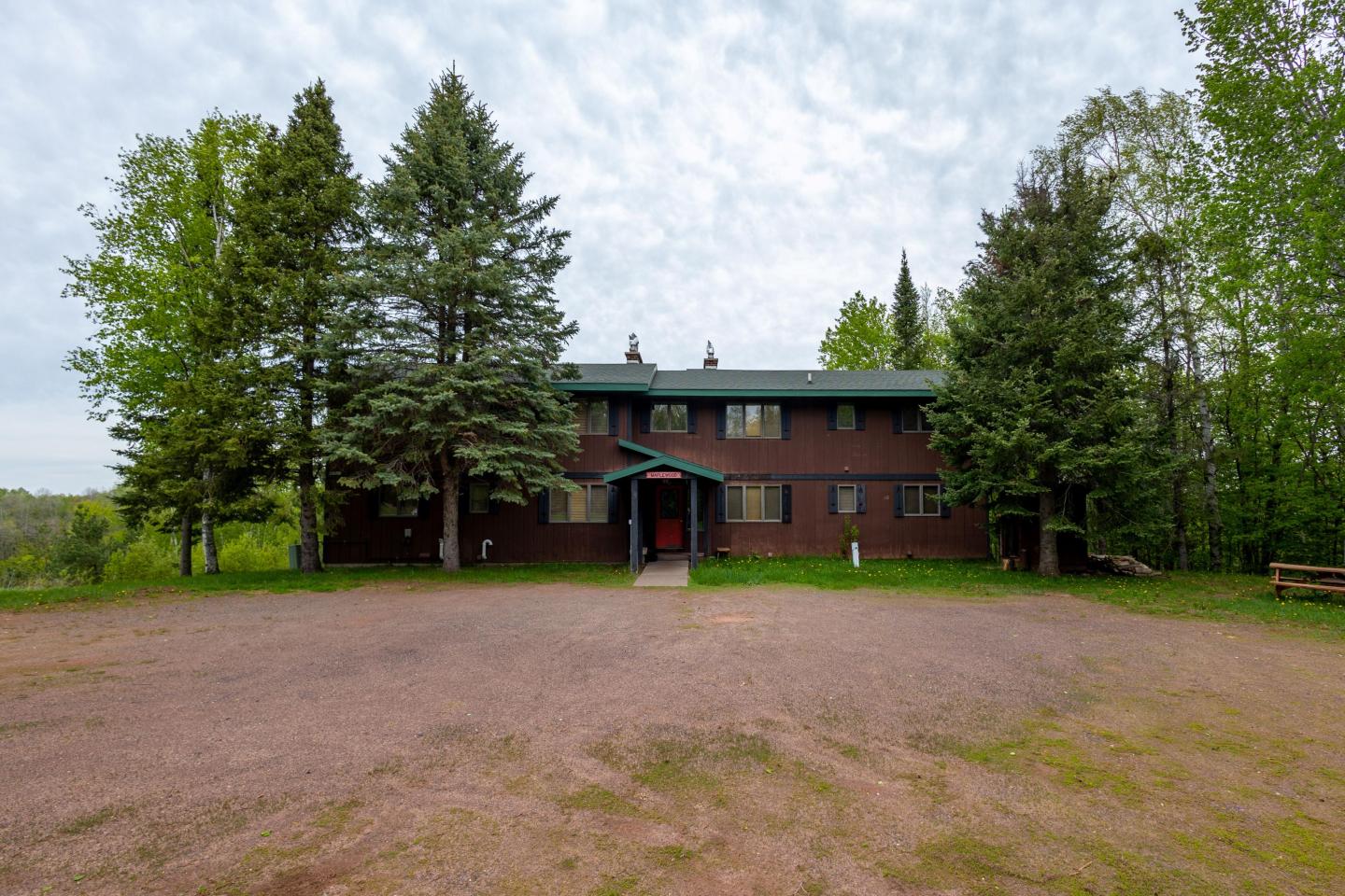 Two-story brown building surrounded by trees under a cloudy sky.