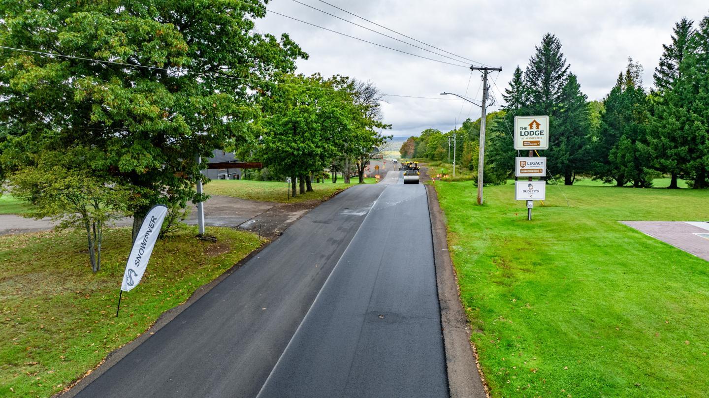 A road flanked by green lawns and trees, under a cloudy sky.