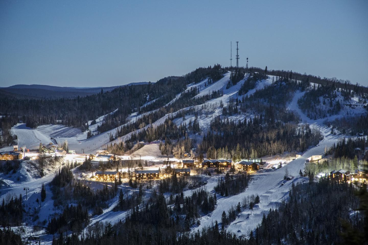 Snowy mountain landscape with ski slopes lit at night.