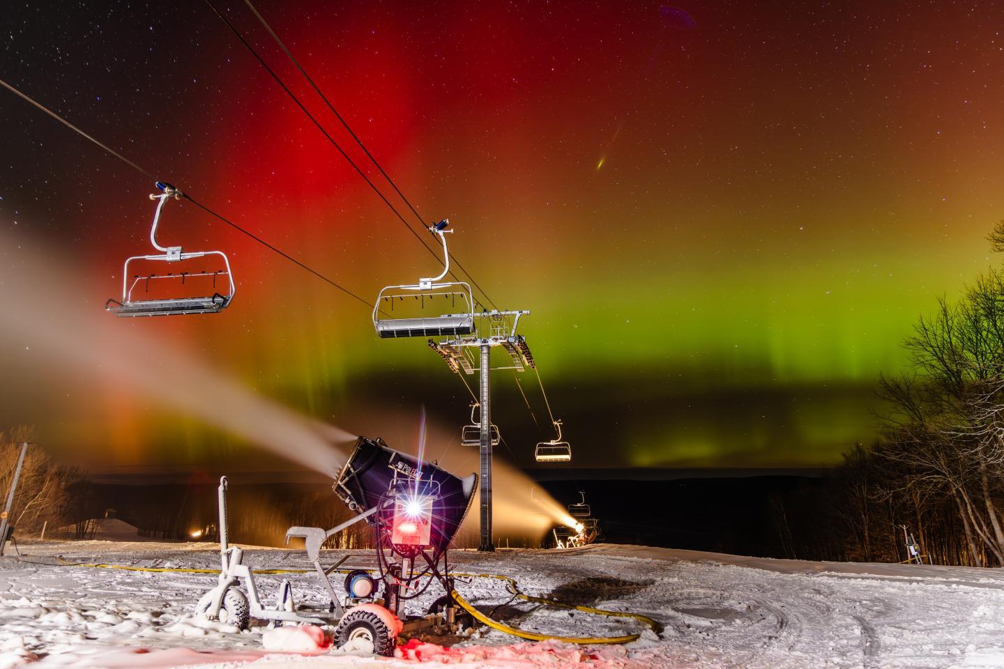Ski lift under vibrant aurora, snowy landscape, and lit snow machine.
