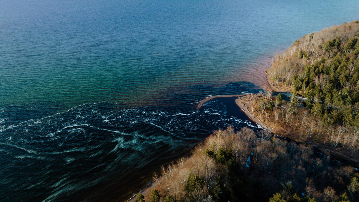Aerial view of river merging with the sea near a forested coastline.