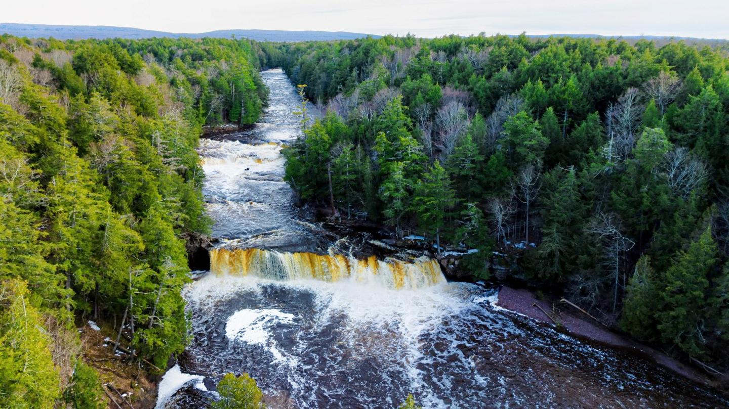 Waterfall flowing through dense green forest from an aerial view.