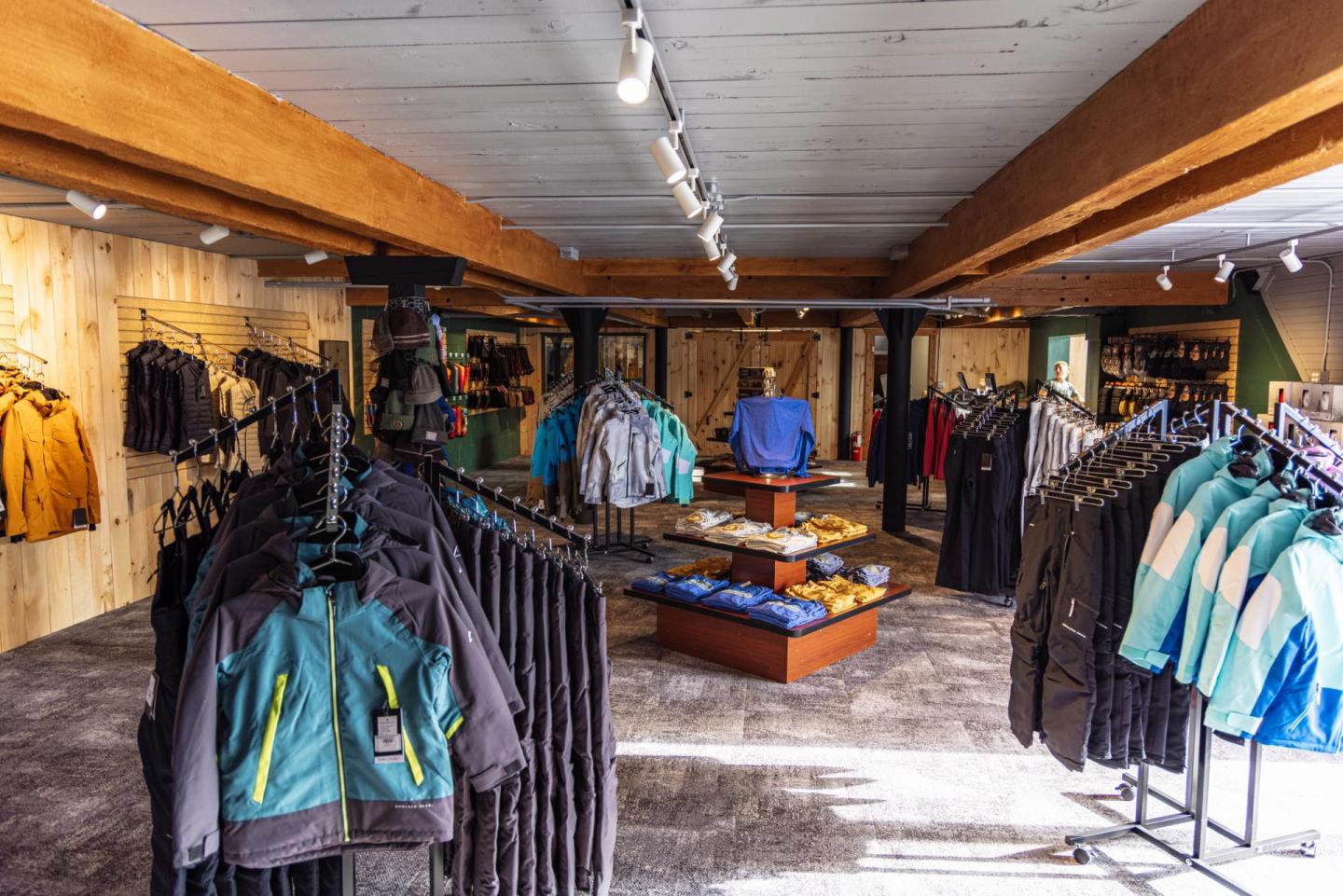 Clothing store interior with racks of jackets and shirts under wooden beams.