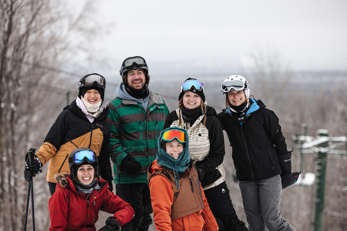 Six skiers posing happily on a snowy slope, wearing colorful winter gear.