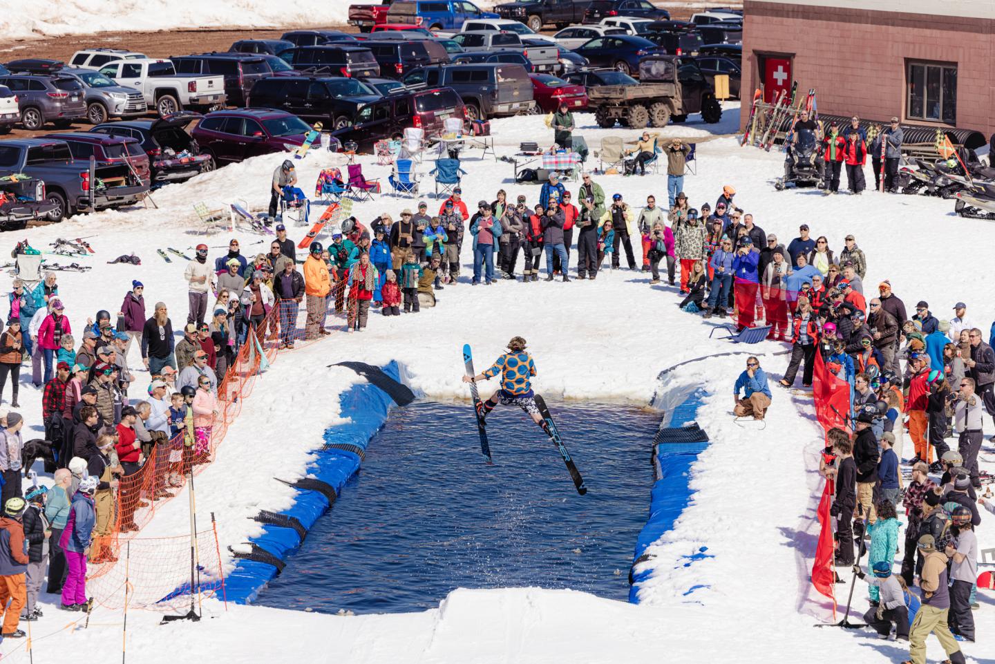 Skier jumping over a snowy pond, crowd cheering.