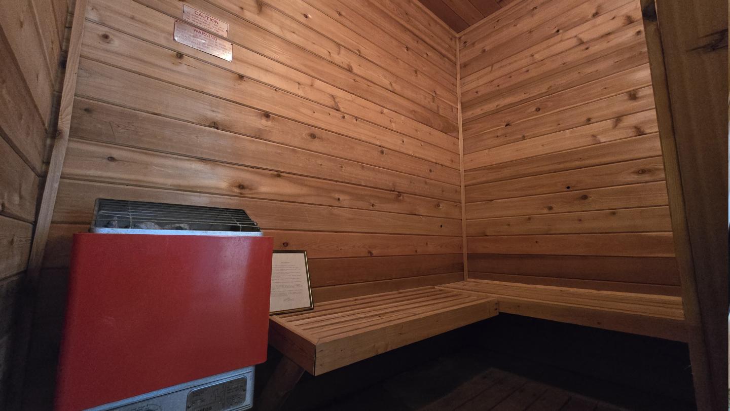 Wooden sauna room with bench, red heater in corner.