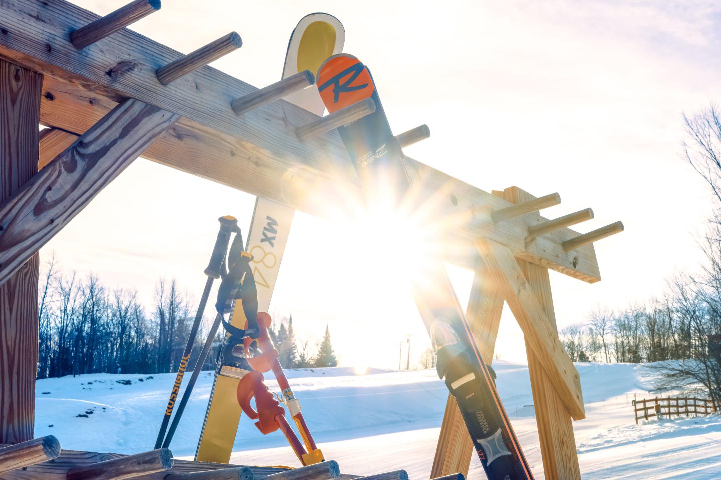 Skis resting on a wooden rack in snowy sunlight.