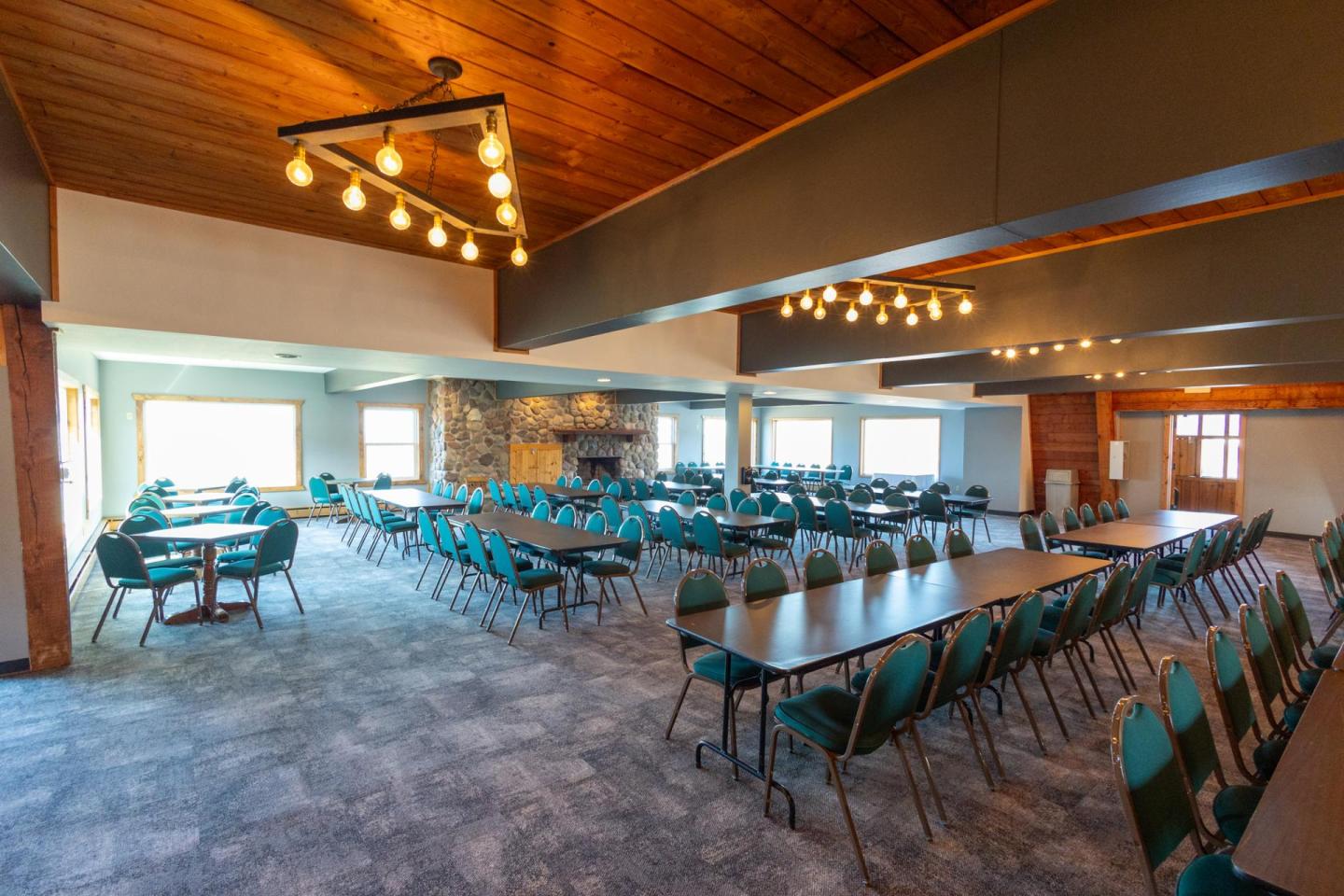 Dining hall with long tables, teal chairs, and a stone fireplace.