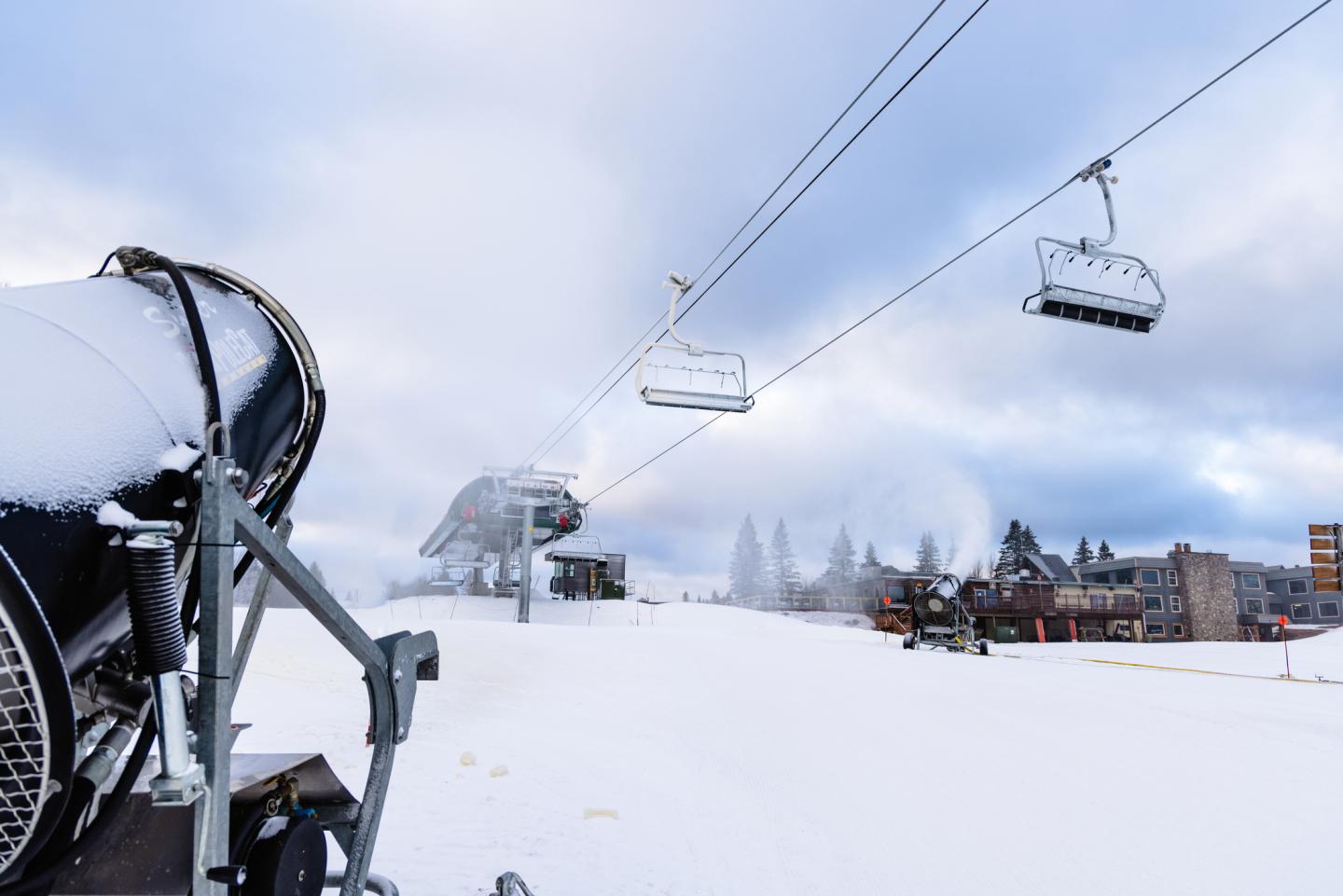 Ski lift chairs over snowy landscape with snow-making machine.