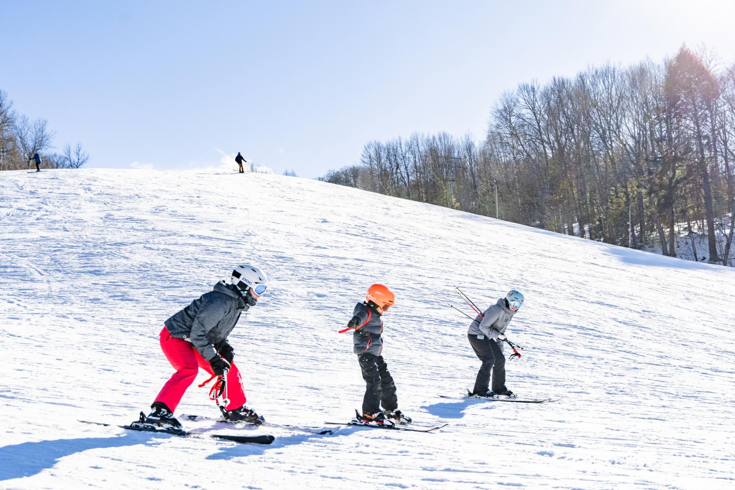 Three people skiing downhill on a sunny day.