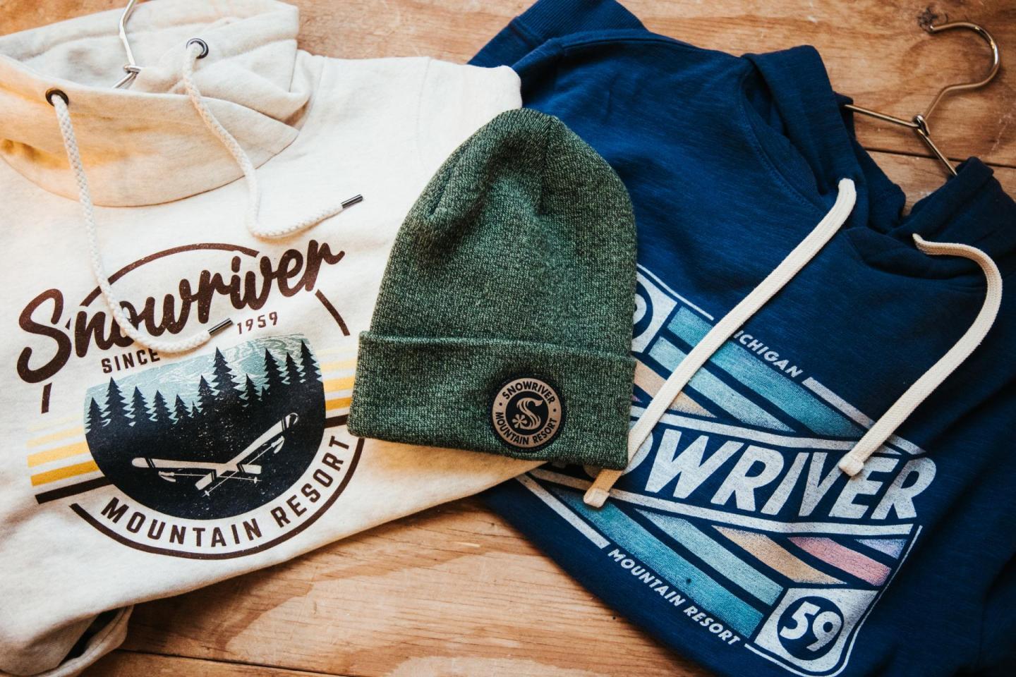 Hoodies and a green knit cap on a wooden surface.