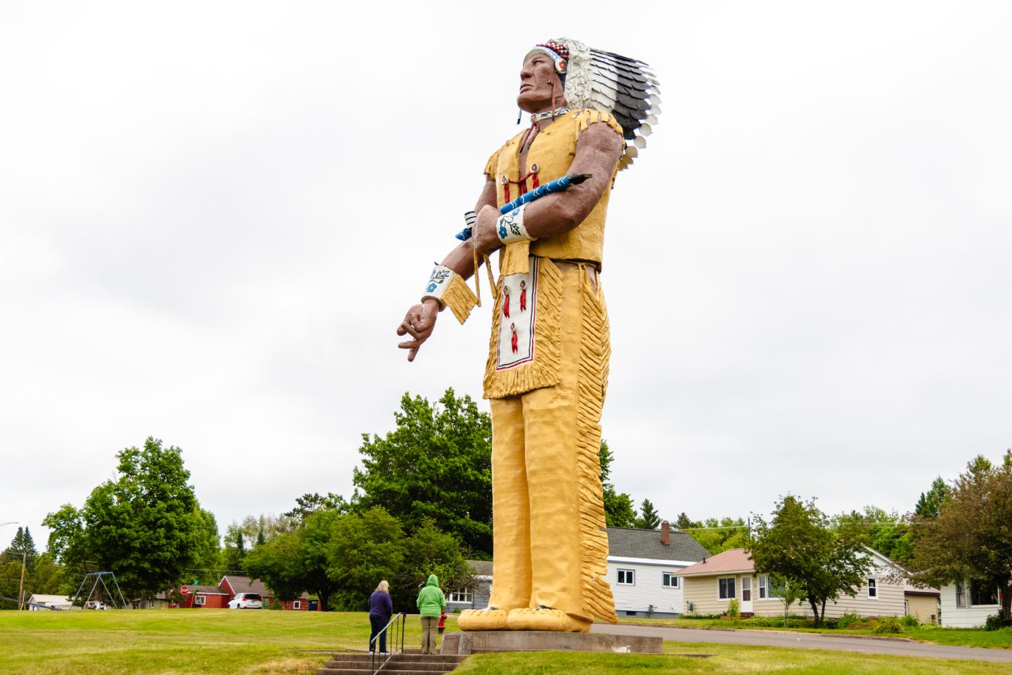 A large Native American statue with headdress and traditional attire stands in a grassy area.
