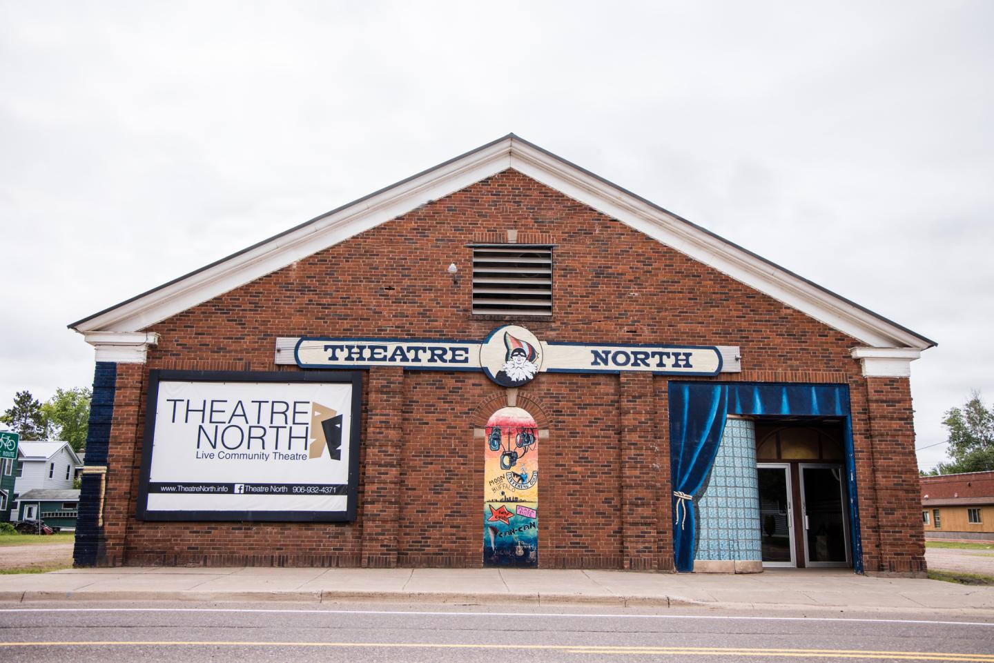 Red brick theater building with a colorful mural and a large sign.