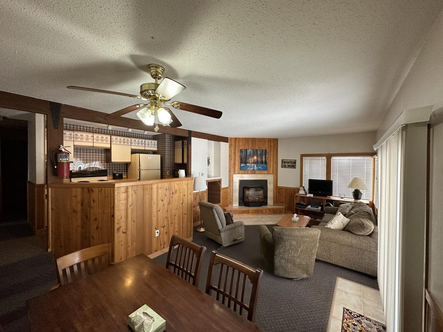 Cozy living room with a fireplace, sofa, and dining area. Warm lighting and wood accents.