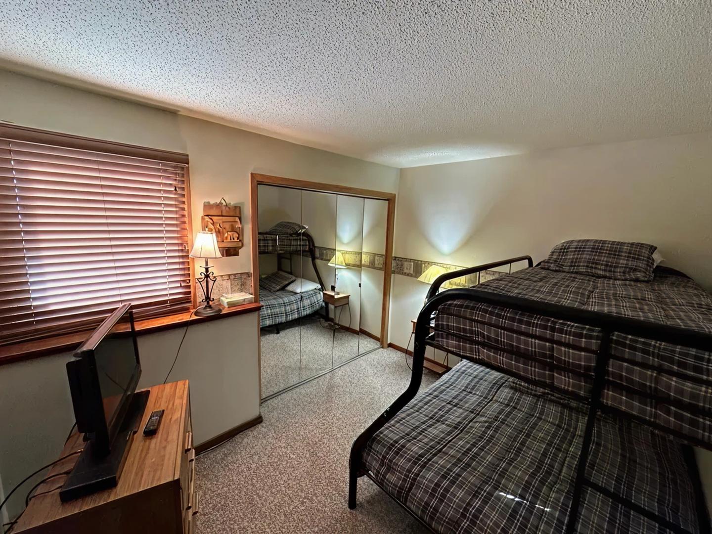 Cozy bedroom with bunk beds, mirrored closet, and a small TV on a wooden dresser.