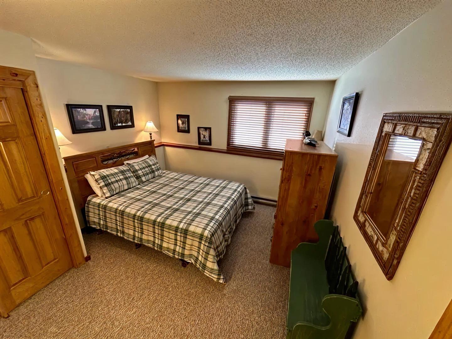 Cozy bedroom with plaid bedspread, pictures, mirror, and wooden furniture.