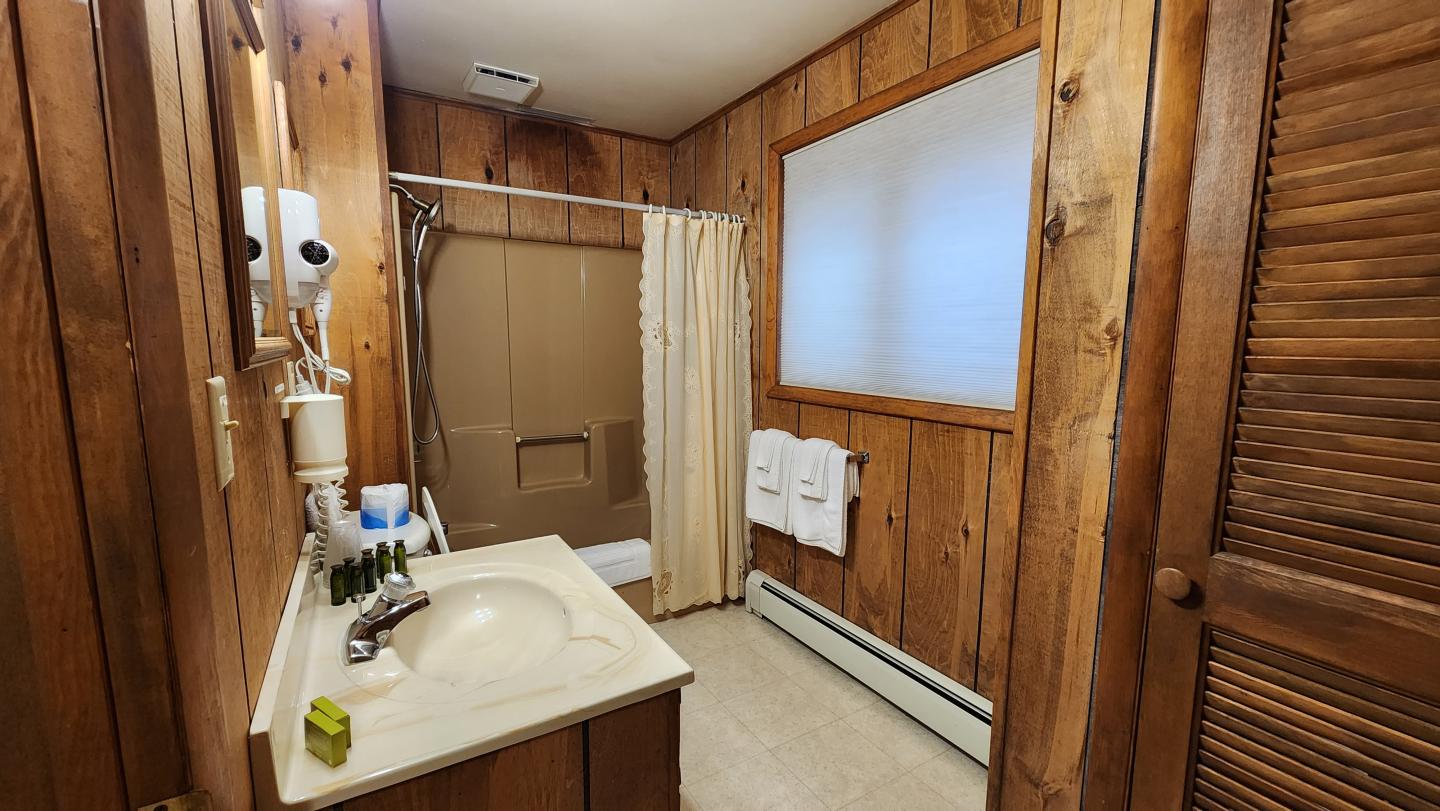 Wood-paneled bathroom with a sink, shower, and towels on the wall.