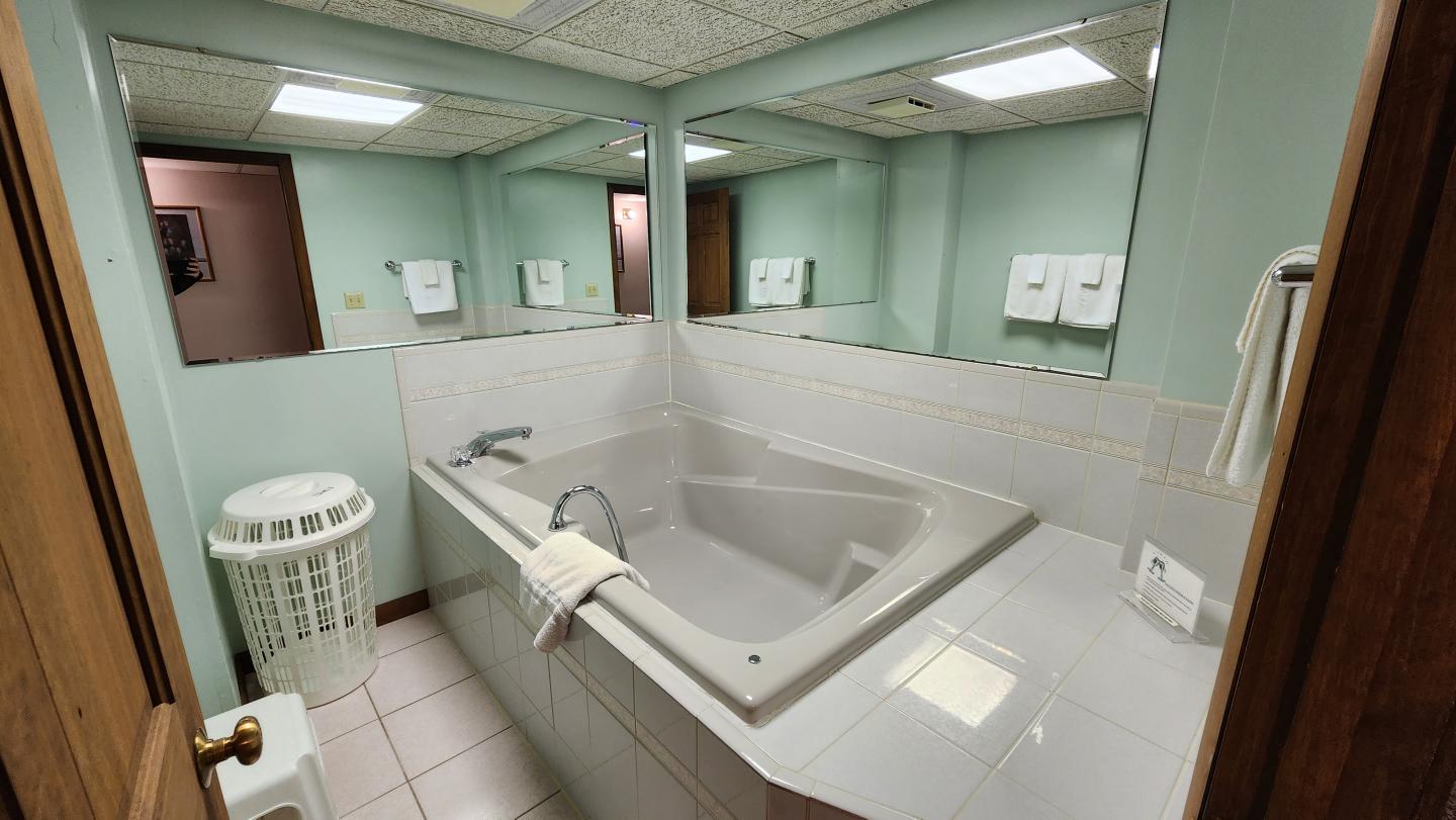 A bathroom with a large corner bathtub, mirrors, and soft lighting.