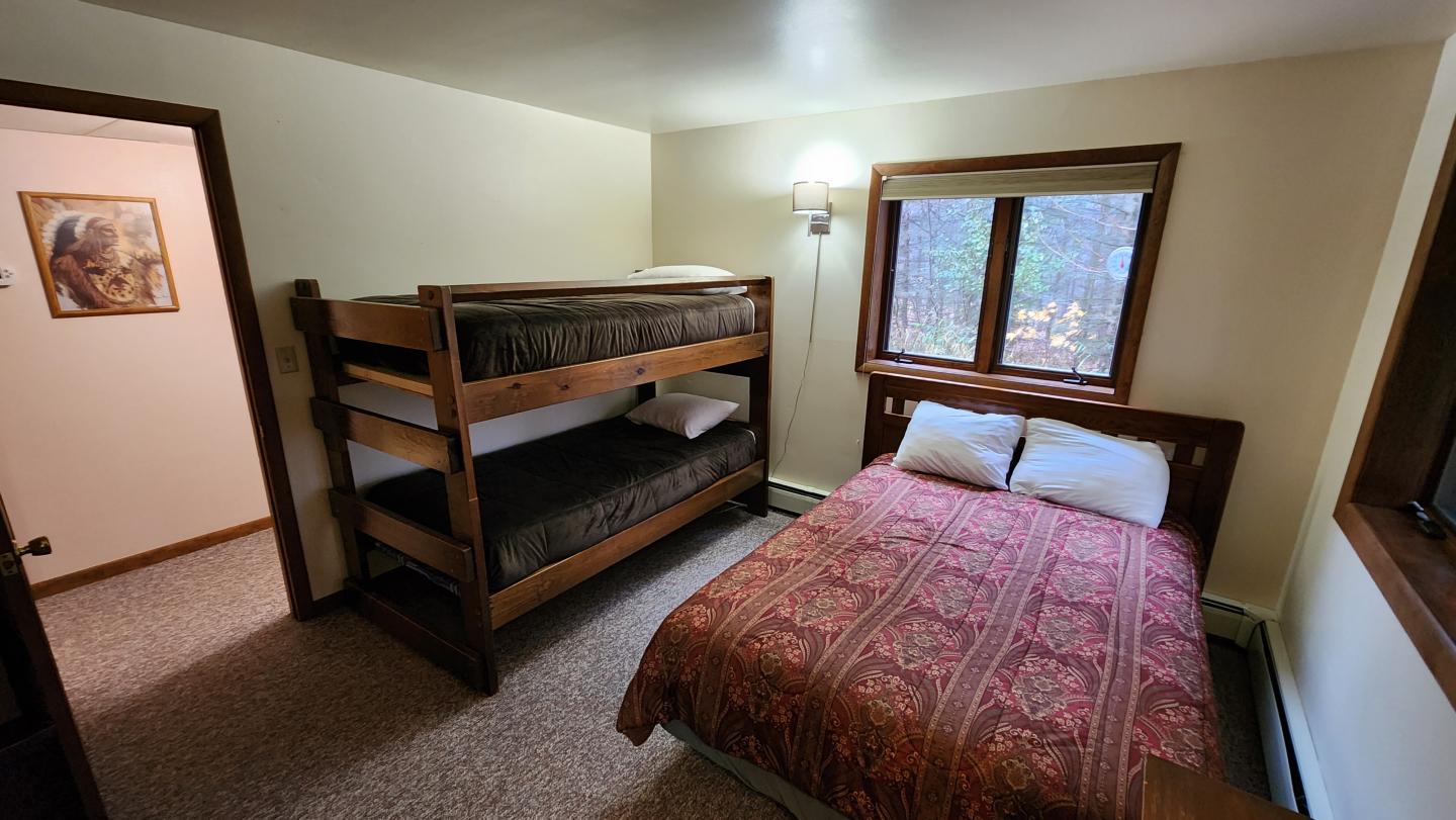 Bunk bed and twin bed in cozy bedroom, window showing trees outside.