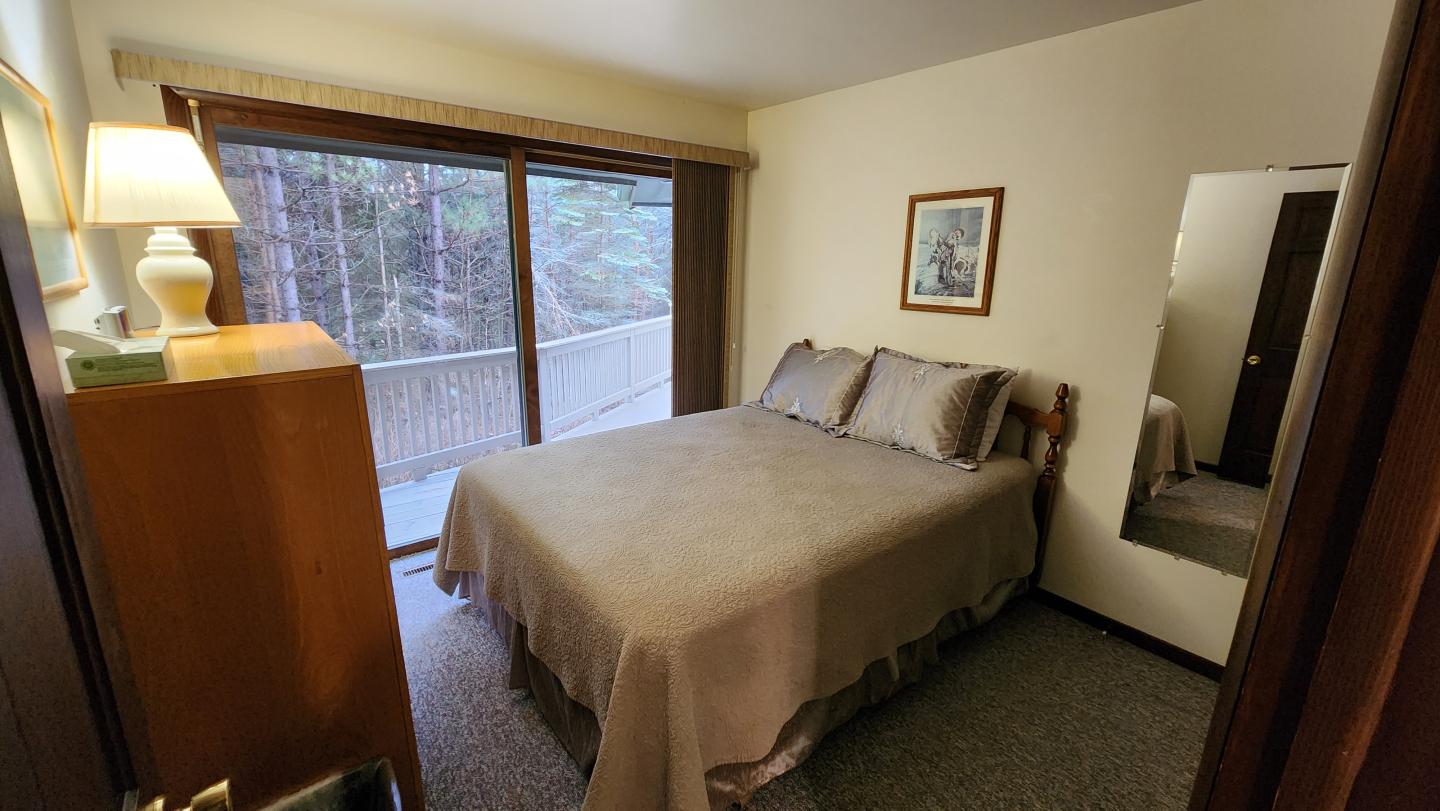 Small bedroom with a large window, beige bedspread, and wooden furniture.