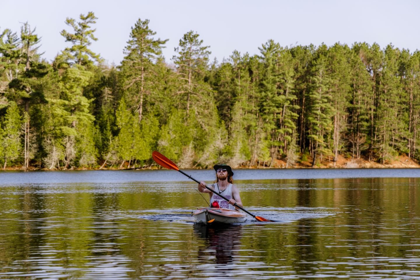 Paddler in a kayak on a calm lake, surrounded by trees.