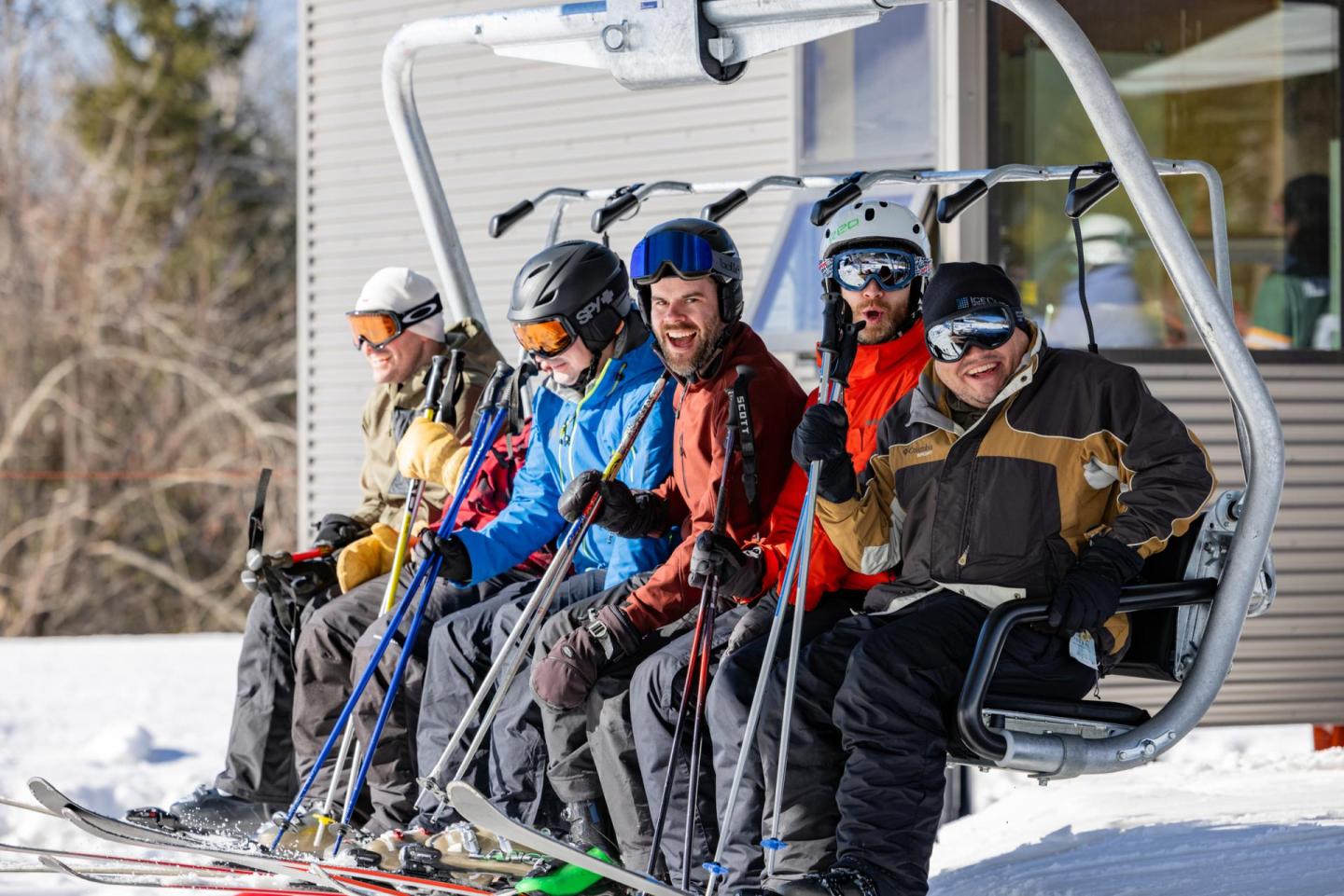Group of skiers on a ski lift, wearing winter gear, enjoying a sunny day.