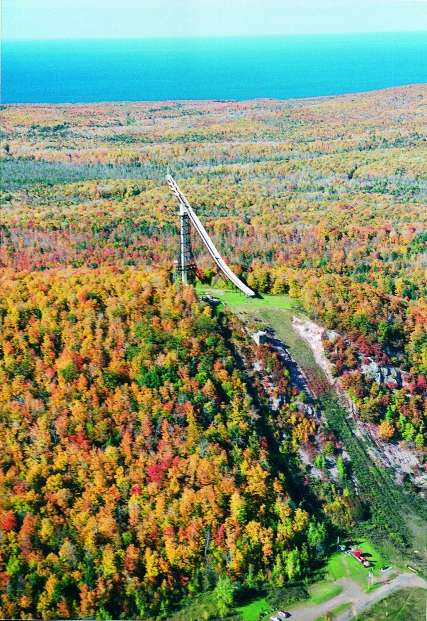 Aerial view of a long bridge over autumnal forest leading to a blue lake.