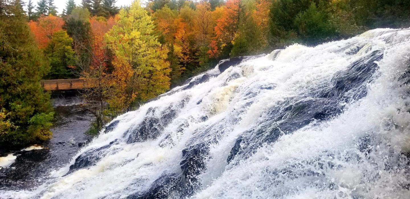 Waterfall cascading beside autumn trees with orange and yellow foliage.