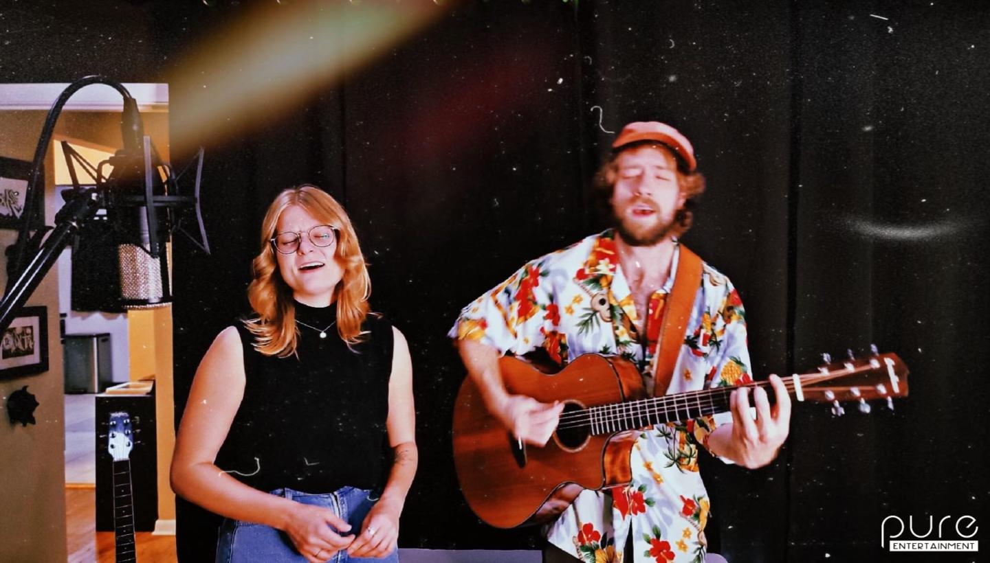 Singers performing in a dimly lit studio, one with a guitar.