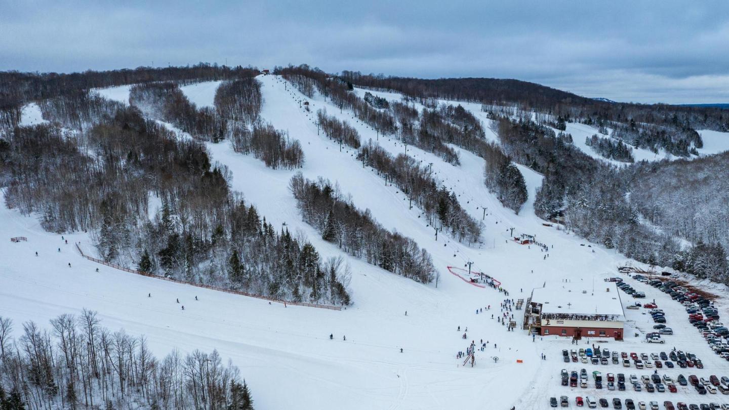 Snowy ski resort with slopes, trees, and a lodge at the base.