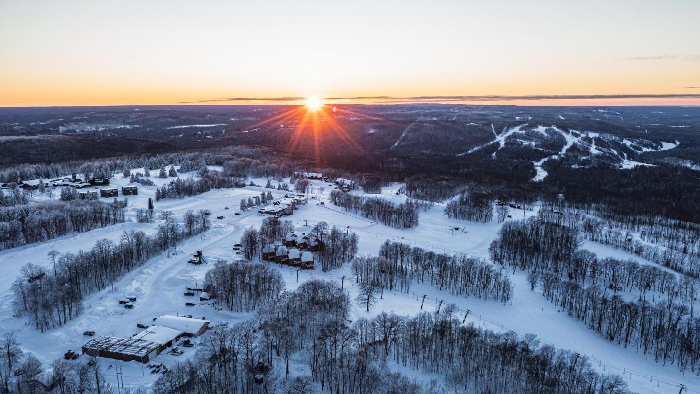 Snowy landscape with a sunset over hills and trees.