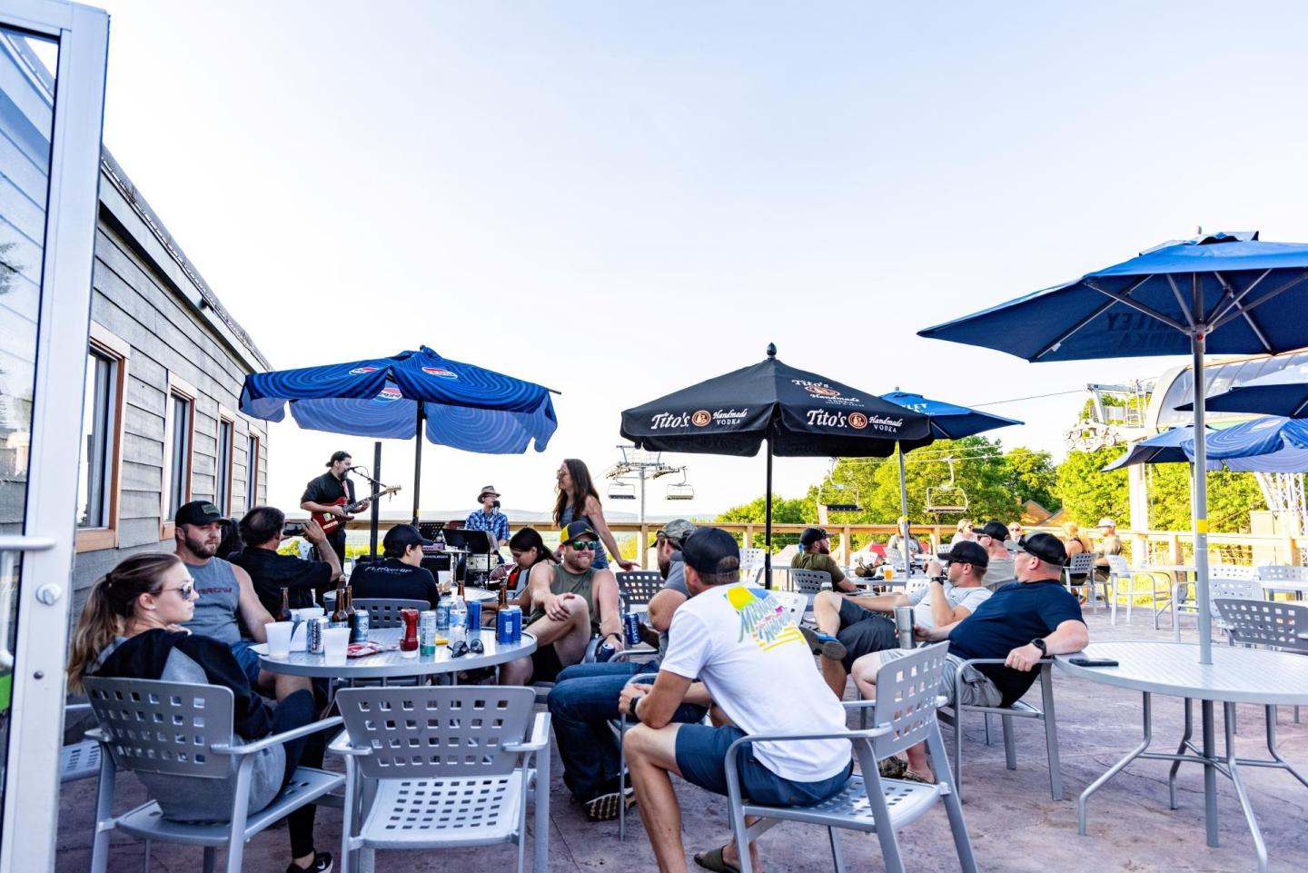Outdoor patio with people sitting under blue umbrellas, enjoying a sunny day.